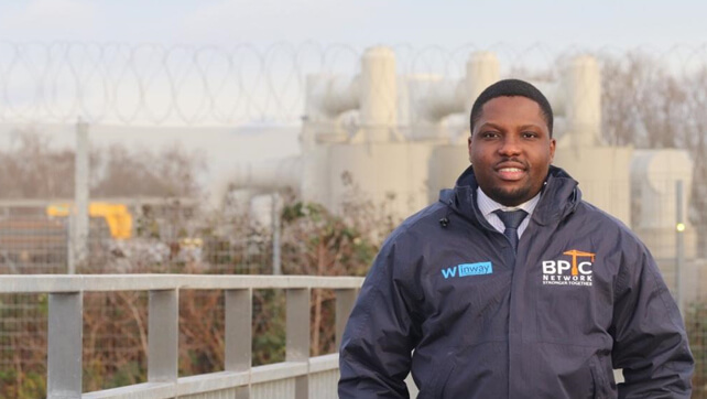 Loughborough alumnus Amos headshot standing in front of an industrial site.